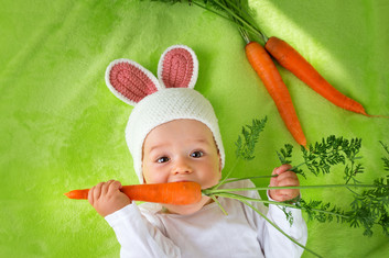 Baby mit Hasenmütze isst eine Karotte.