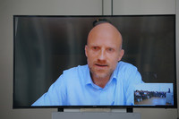 Auf einem großen Bildschirm ist Stefan Storcksdieck genannt Bonsmann zu sehen und hält einen Vortrag via Videokonferenz.
