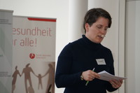 Moderatorin Joy Ladurner blickt auf ein Moderationskärtchen. Im Hintergrund ist das Roll-Up vom Fonds Gesundes Österreich zu sehen.