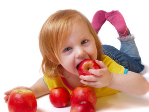 Mädchen isst einen vor ihr liegenden Äpfel.