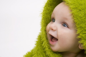 Lachendes Baby mit grüner Decke über den Kopf.