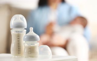 Mutter hält Kind, im Fokus sind Fläschchen mit Säuglingsnahrung