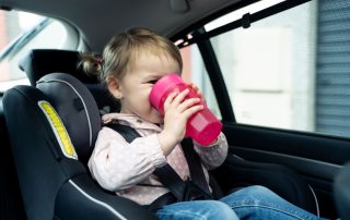 Mädchen sitzt im Auto und trinkt aus einem pinkfarbenen Becher