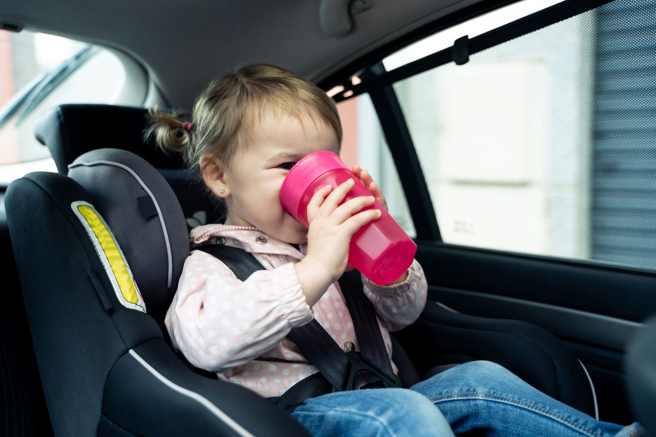 Mädchen sitzt im Auto und trinkt aus einem pinkfarbenen Becher